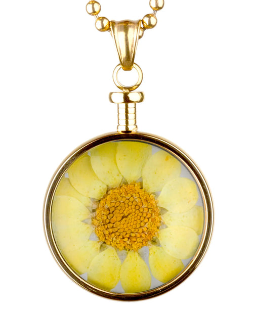 goldfarbener anhänger mit gelber blume hinter glas